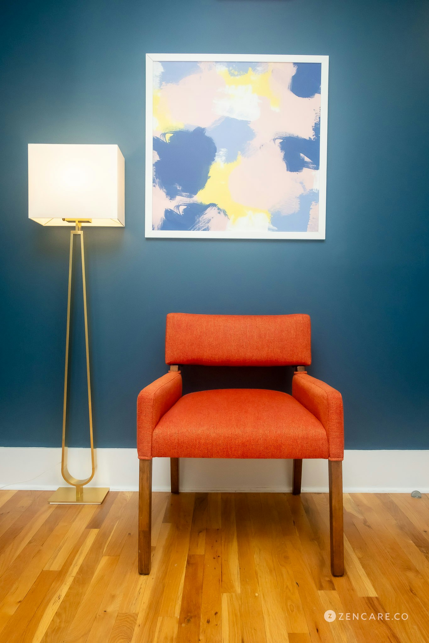 Warm therapeutic space with modern orange chair against a navy blue wall, washed with the yellow light of a hanging lamp